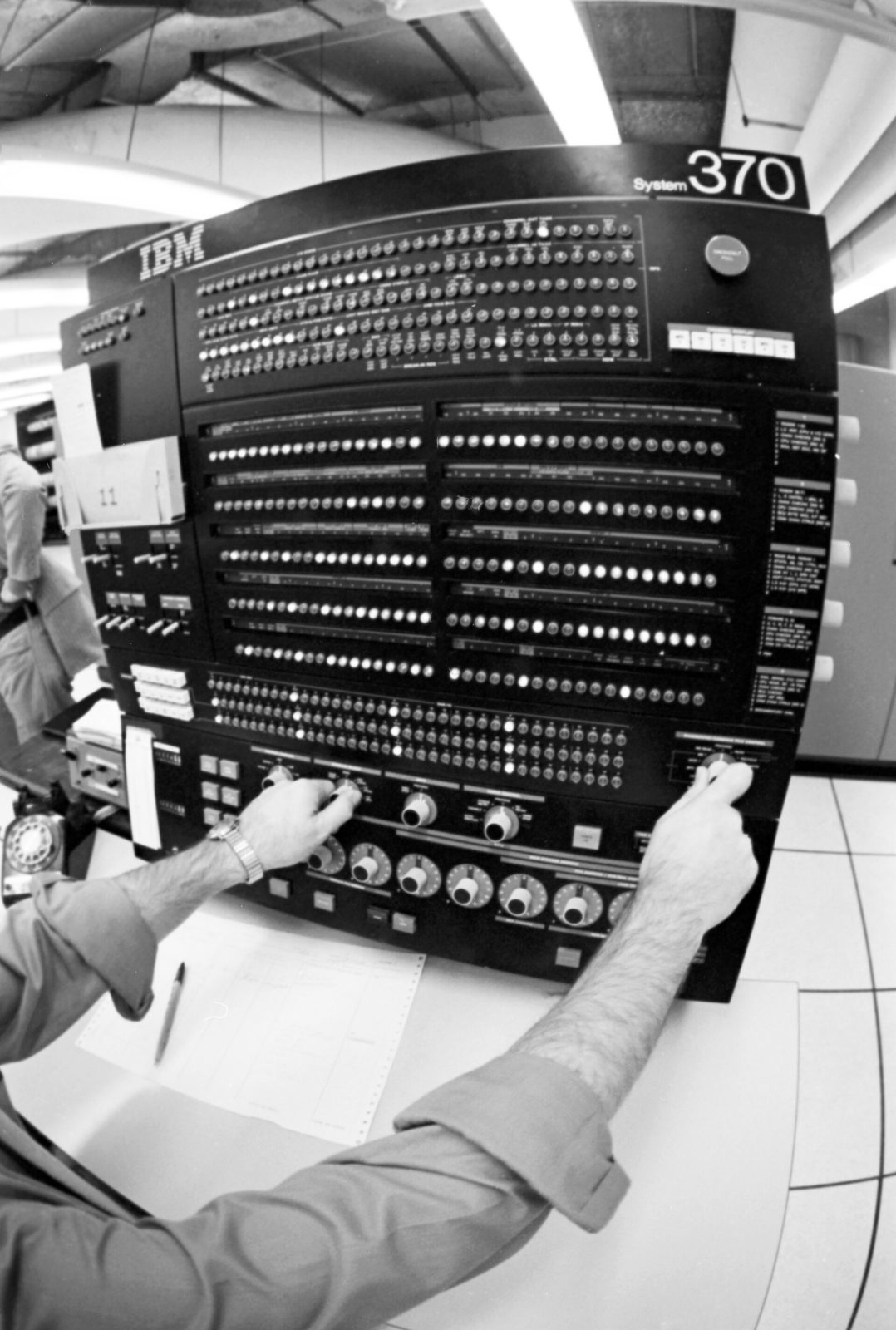 Ruce operátora na ovládacím panelu počítače IBM 370 s mnoha kontrolkami