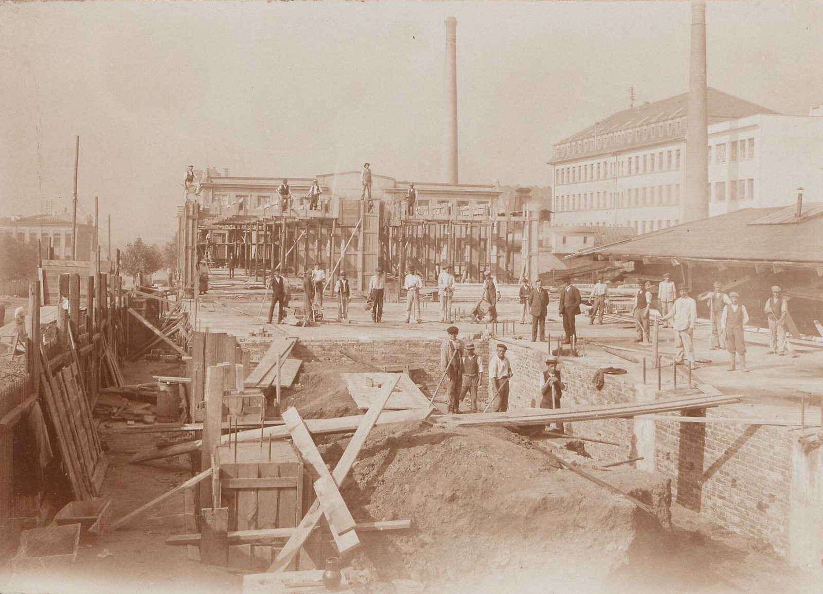 Stavba továrny Waldes a spol. ve Vršovicích kolem roku 1920 - dělníci na staveništi, komíny v pozadí