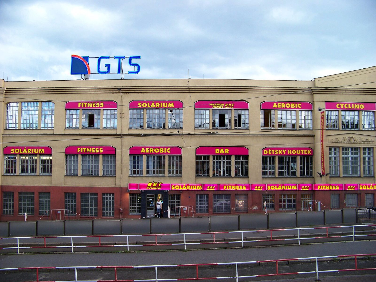 Průčelí bývalé papírny s růžovými reklamami fitness centra a neonem GTS